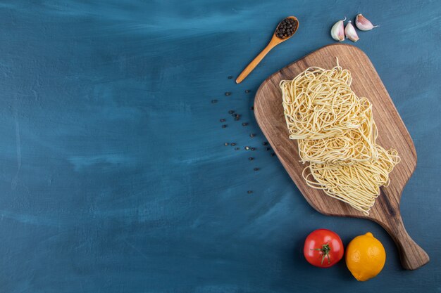 Una tavola di legno di spaghetti crudi con pomodoro rosso fresco e limone su sfondo blu ..