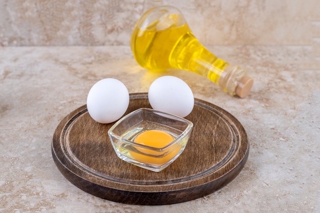 Una tavola di legno di uova crude e una bottiglia di olio di vetro