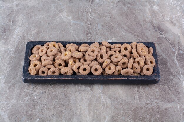 Una tavola di legno nera di anelli di cereali al cioccolato sani per la colazione.