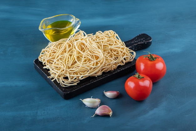 Una tavola di legno nera di spaghetti crudi su sfondo blu.