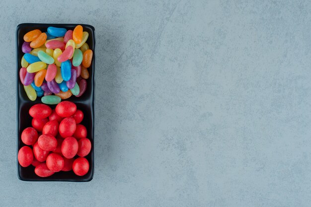 Una tavola di legno nera piena di caramelle colorate di fagioli su una superficie bianca