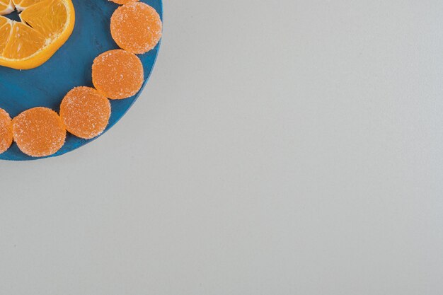 Una tavola di legno piena di caramelle di gelatina zuccherina e una fetta di arancia.