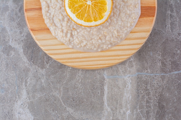 Una tavola di legno piena di farina d'avena con una fetta d'arancia.