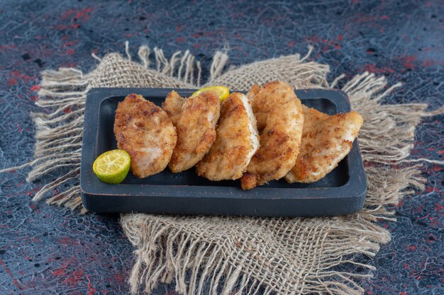 Una tavola di legno scuro con carne di pollo al forno con fettine di limone.