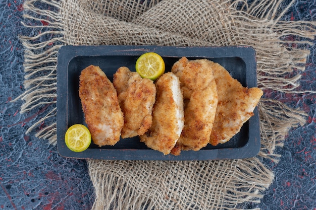 Una tavola di legno scuro con carne di pollo al forno con fettine di limone.