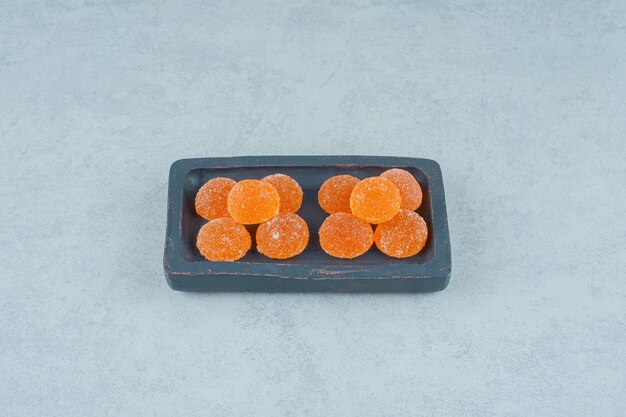Una tavola di legno scuro piena di caramelle di gelatina di arancia dolce su una superficie bianca
