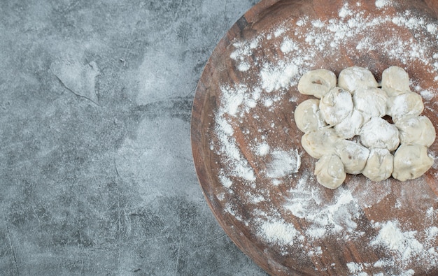 Una tavola rotonda di legno con gnocchi crudi e farina.