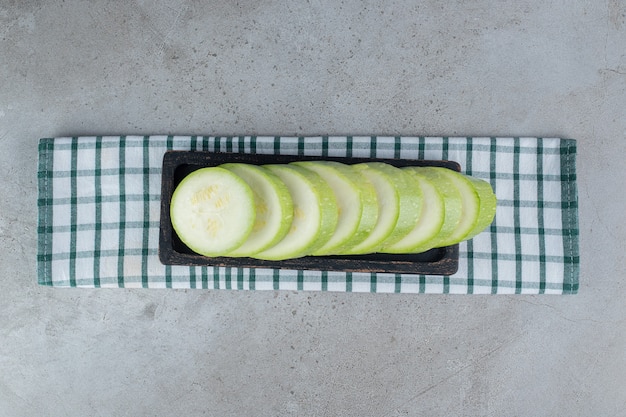 Una tavola scura con zucchine a fette su uno sfondo grigio. Foto di alta qualità