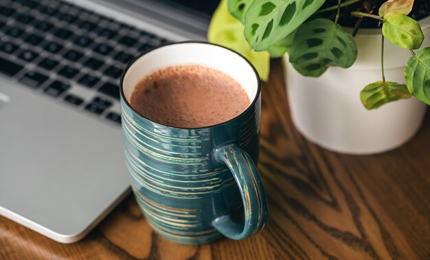 Una tazza di cacao un computer portatile e un vaso di fiori sul primo piano del desktop