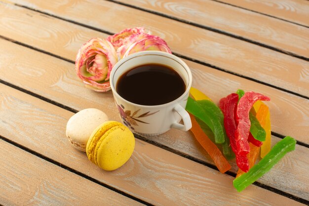 Una tazza di caffè caldo e forte con vista dall'alto con fiori di macarons francesi e marmellata sulla scrivania rustica color crema bere caffè foto biscotto dolce