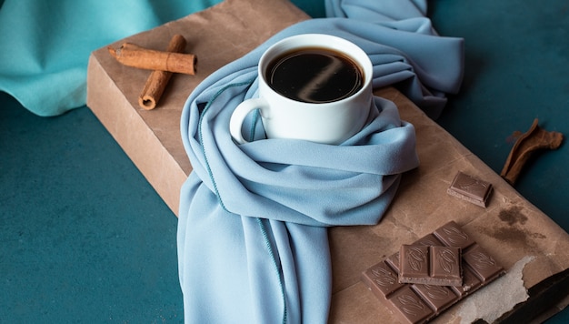 Una tazza di caffè con bastoncini di cannella e barretta di cioccolato.