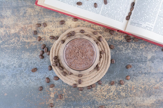 Una tazza di caffè con libro aperto e chicchi di caffè su sfondo marmo. Foto di alta qualità