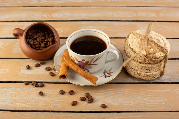 Una tazza di caffè con vista frontale calda e forte con semi di caffè marroni freschi cannella e cracker sulla scrivania rustica crema di semi di caffè bevanda foto grano