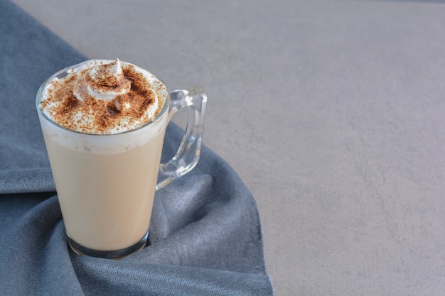 Una tazza di caffè delizioso caldo decorato con cacao su panno blu.