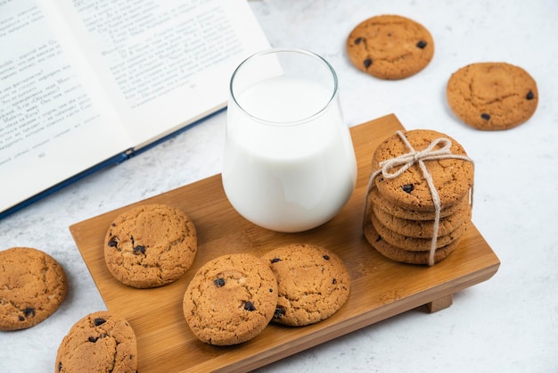 Una tazza di latte con biscotti al cioccolato su un tagliere di legno.