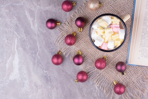 Una tazza di marshmallow con palline rosse dell'albero di Natale intorno