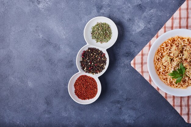 Una tazza di spaghetti con spezie intorno.