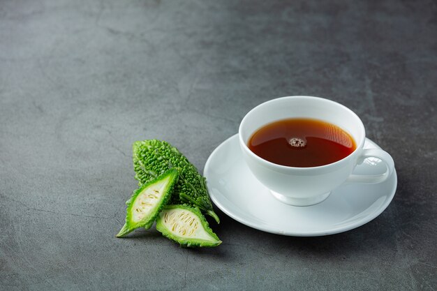 una tazza di tè caldo alla zucca amara con una zucca amara cruda a fette sul pavimento scuro