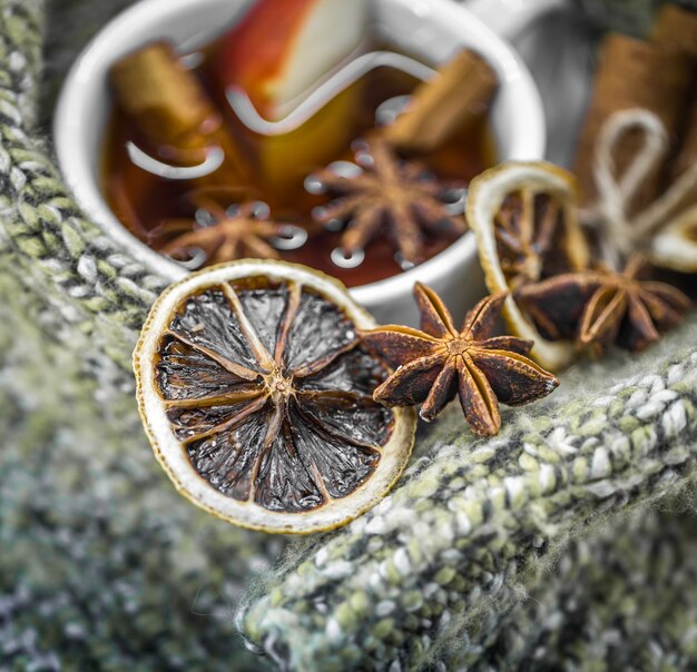 una tazza di tè caldo con bastoncini di cannella, spezie e delizioso limone essiccato su legno con un maglione caldo