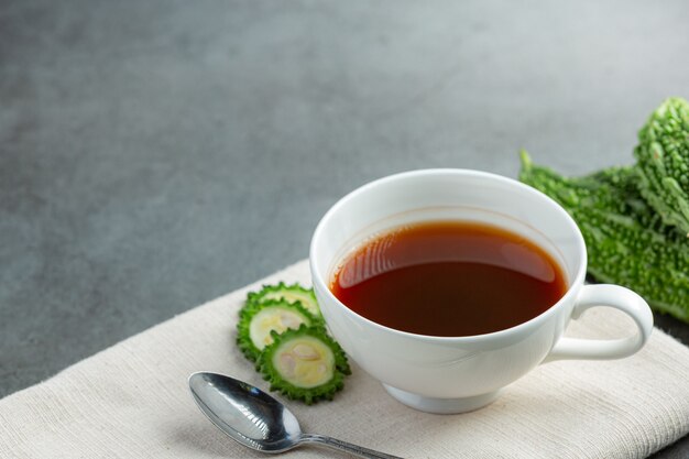 una tazza di tè caldo zucca amara con posto zucca amara a fette crudo su tessuto bianco