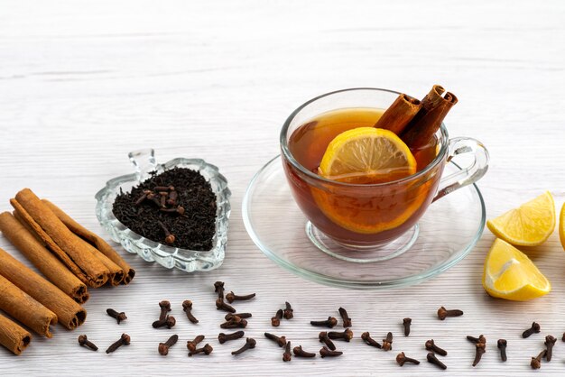 Una tazza di tè con vista frontale al limone e cannella su bianco, caramella dolce del tè