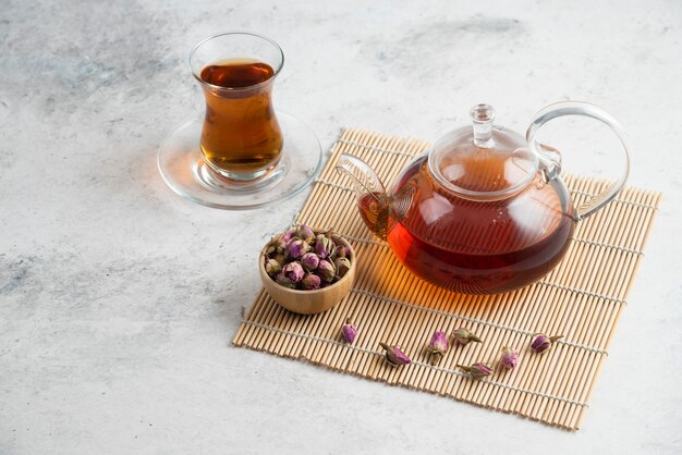 Una tazza di tè di vetro con rose essiccate e teiera