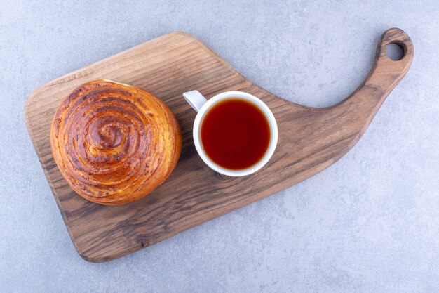 Una tazza di tè e un panino dolce su una tavola di legno su una superficie di marmo