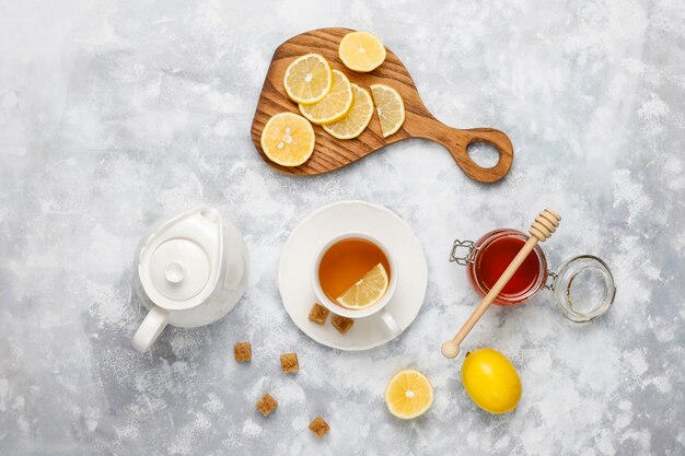 Una tazza di tè, zucchero di canna, miele e limone su cemento. Vista dall'alto, copia spazio