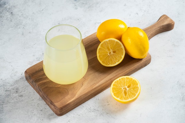 Una tazza di vetro di succo di limone fresco su una tavola di legno.