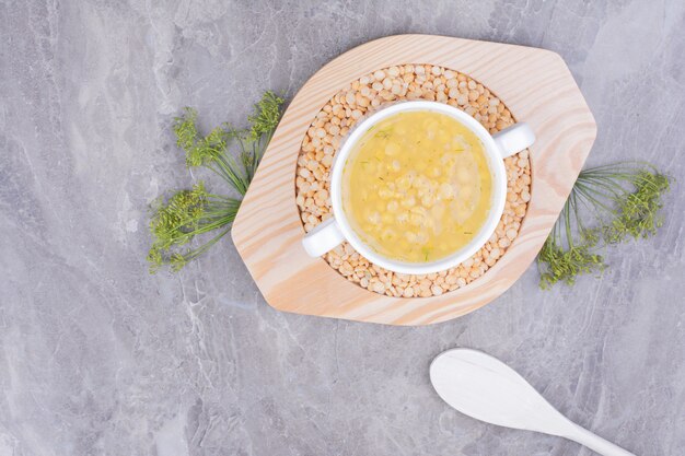 Una tazza di zuppa di piselli su fagioli crudi in un piatto di legno.