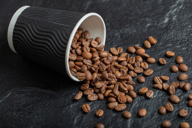 Una tazza nera piena di chicchi di caffè sulla tavola di legno.