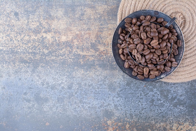 Una tazza scura piena di chicchi di caffè su marmo