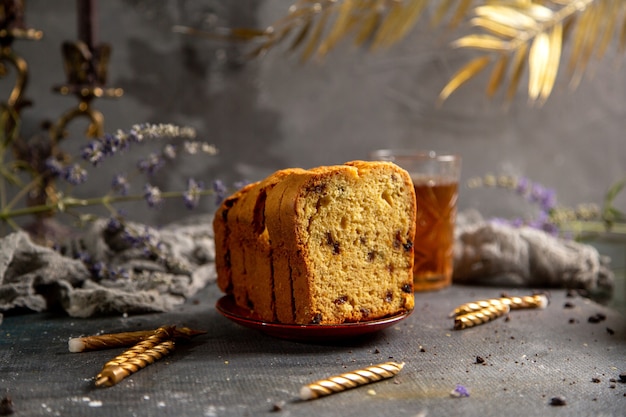 Una torta al forno vista frontale con candele fiori viola e tè sulla scrivania grigia