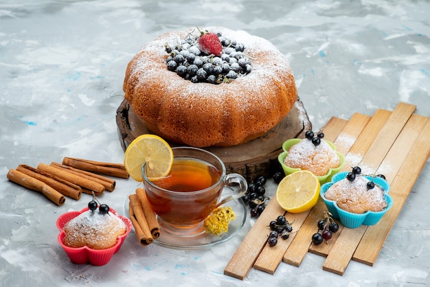 Una torta alla frutta vista frontale deliziosa e rotonda formata con blu fresco, frutti di bosco e insieme a una tazza di tè su zucchero dolce e dolce