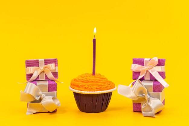 Una torta arancione di vista frontale con la candela e contenitori di regalo viola sul giallo, festa di compleanno del biscotto