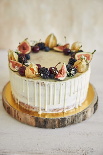 Una torta di compleanno fruttata con topper di compleanno, frutta in cima e gocciolamento bianco su sfondo beige