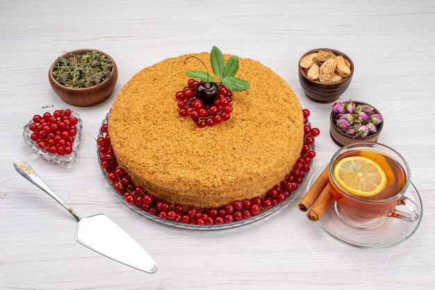 Una torta di miele rotonda con vista dall'alto deliziosa e al forno con mirtilli rossi e tè sulla foto grigia dello zucchero del biscotto della torta della scrivania