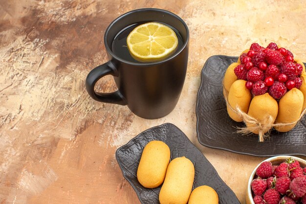 Una torta e un tè del regalo in una tazza nera con limone e biscotti sulla vista ravvicinata della tabella dei colori misti