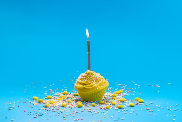 Una torta gialla di vista frontale con la candela sulla torta blu della caramella di colore dello scrittorio