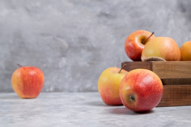 Una vecchia scatola di legno piena di frutti maturi freschi di mela rossa posizionati su uno sfondo di marmo. Foto di alta qualità