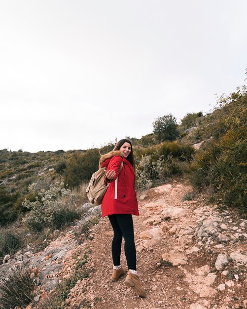 Una viandante femminile con il suo zaino che cammina sul sentiero di montagna