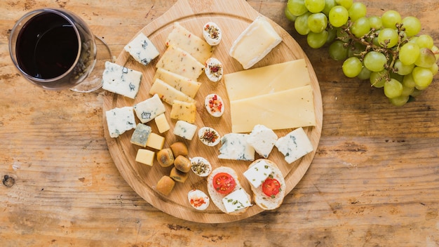 Una vista aerea del bicchiere di vino rosso con blocchi di formaggio e pomodori sullo scrittorio di legno