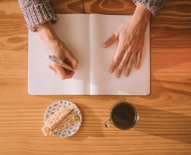 Una vista aerea della donna che scrive sul taccuino bianco vuoto con penna e colazione sul tavolo