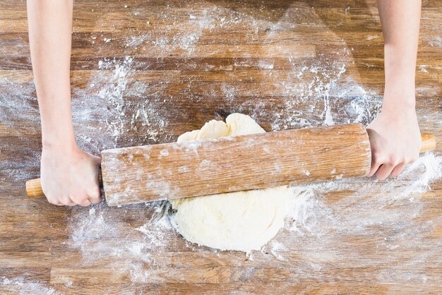 Una vista aerea della mano della donna che appiattisce la pasta con i matterelli sullo scrittorio di legno