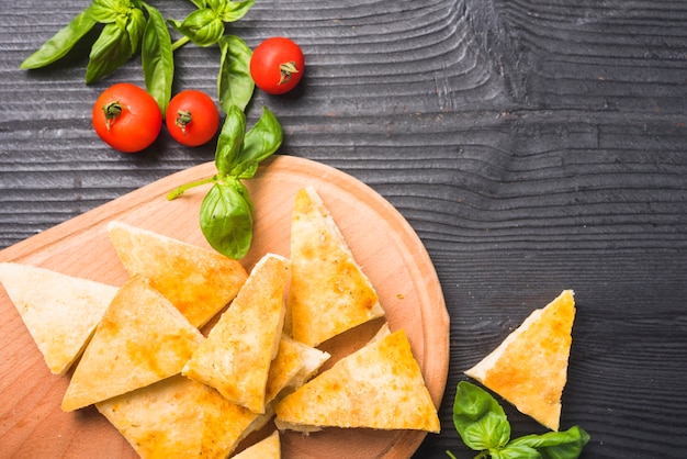 Una vista aerea delle fette di pane con foglie di basilico e pomodori sul tavolo di legno