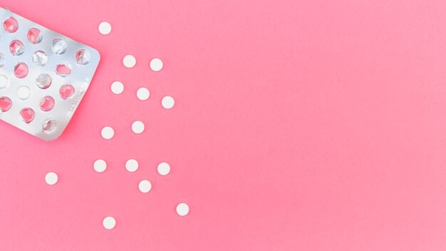 Una vista aerea delle pillole rotonde bianche fuori dal blister su sfondo rosa