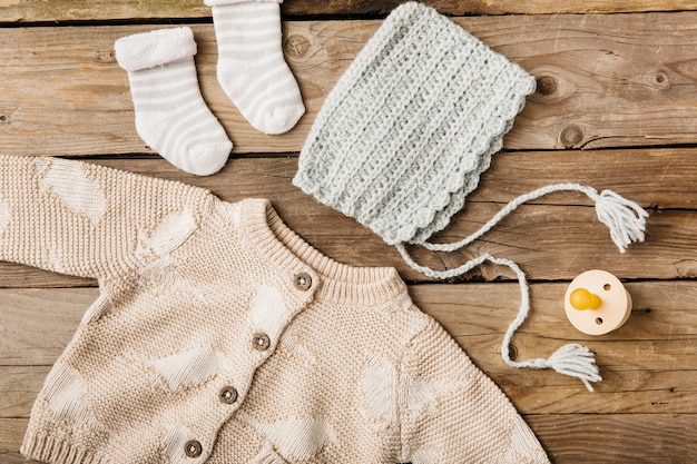 Una vista aerea di abbigliamento del bambino di lana con ciuccio sul tavolo di legno