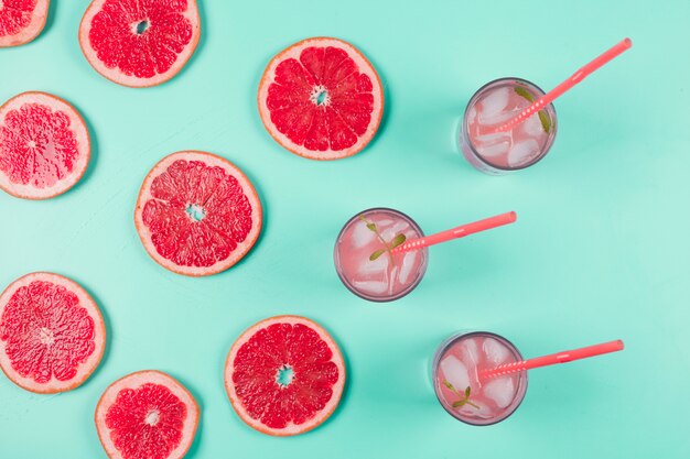 Una vista aerea di fette di pompelmo e bicchiere di succo con ghiaccio e menta su sfondo pastello