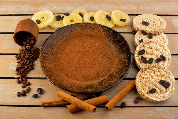 Una vista dall'alto caffè in polvere marrone all'interno della piastra nera con ananas essiccato cannella e cracker sulla crema tavolo rustico caffè seme bevanda foto grano