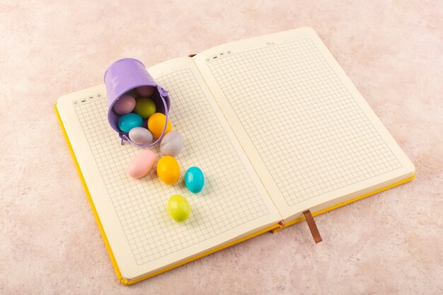 Una vista dall'alto caramelle colorate sparse su tutto il quaderno e caramelle rosa da scrivania color zucchero dolce